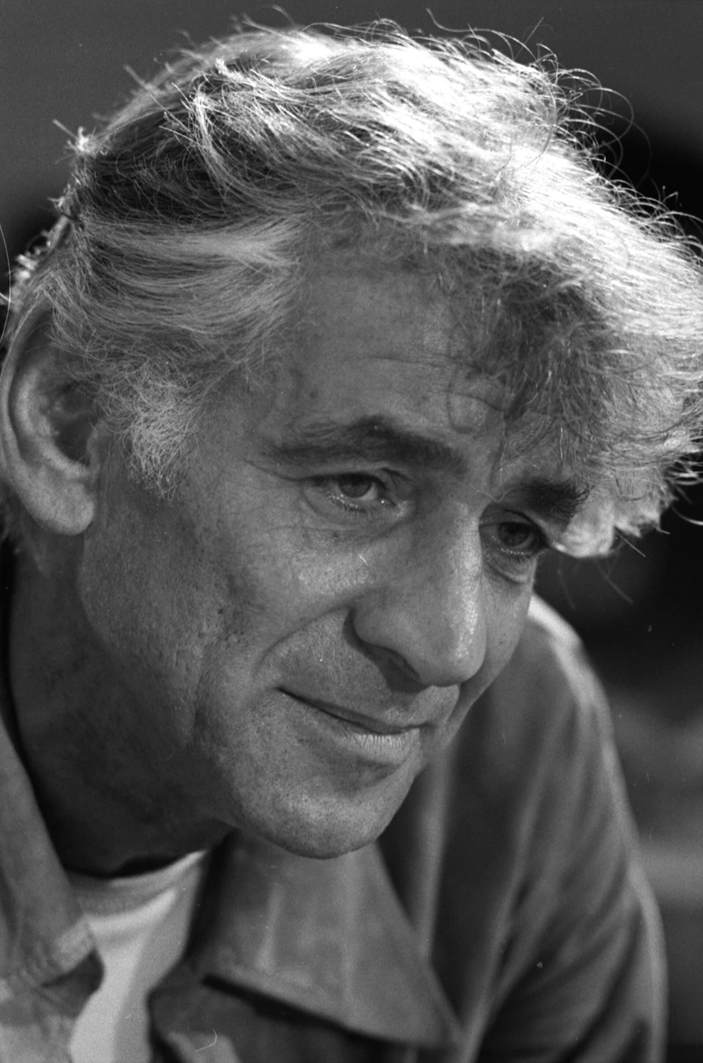 Close black and white portrait of Leonard Bernstein in 1971, grey hair swept back, half smiling and looking off to one side.